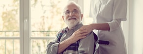 A caregiver supports an elderly man in a wheelchair by the window, emphasizing medbridge's role in healthcare training.
