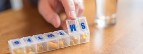 A hand uses a weekly pill organizer, highlighting digital healthcare's role with a medbridge mention, as water sits nearby.