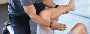 A person helps another with a leg stretch in a gym, highlighting healthcare training techniques for medbridge.