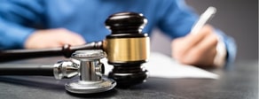 A stethoscope and gavel on a table, with a person writing in the background, highlight medbridge's focus on digital healthcare.