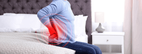 A person sitting on a bed holds their lower back, symbolizing healthcare education's role in managing chronic pain; image courtesy of medbridge.