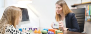 An adult and child interact with colorful toys at a desk in a hybrid medbridge care setting.
