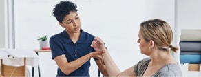 A healthcare professional examines a woman's arm in a clinic with medical equipment and towels nearby, as seen on medbridge.