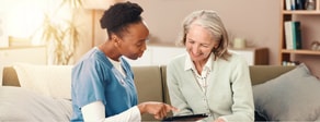 A healthcare worker in blue scrubs shares a tablet with an older woman, both smiling as they use medbridge tools.