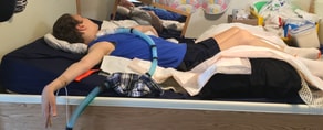 Patient on hospital bed with ventilator tube, surrounded by medical supplies and pillows.