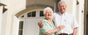 Senior couple smiling in front of house with white doors and windows for medbridge.
