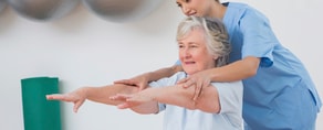A nurse uses Medbridge software to help an elderly woman with arm exercises during physical therapy.