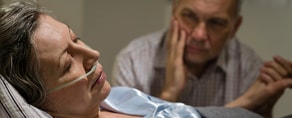 A man sits beside a woman in bed with an oxygen tube, illustrating medbridge's hybrid care approach.