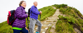 Two people with backpacks hike up a stone path with hiking poles near Medbridge.