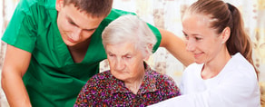 Two healthcare workers in uniforms assist an elderly woman with white hair, highlighting digital healthcare advancements from Medbridge.