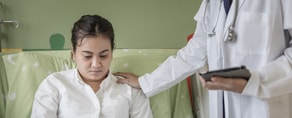 A healthcare professional supports a seated patient while using medbridge software on a clipboard.