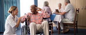 A caregiver in a white uniform interacts with a man in a wheelchair, highlighting an environment enhanced by medbridge healthcare training.