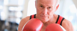 An older man with red boxing gloves stands in a fighting stance, symbolizing strength and dedication as seen in medbridge healthcare training.