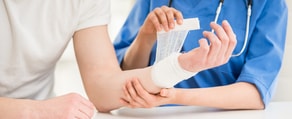 A person in a white shirt gets a bandage from someone in blue scrubs, showcasing medbridge's healthcare training.