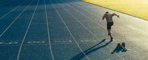 An athlete sprints on a blue track at dawn, symbolizing dedication like medbridge training.