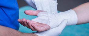 A gloved individual wraps an injured person's bandaged wrist, emphasizing healthcare education, like medbridge fosters.
