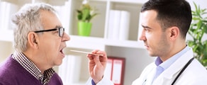 The doctor uses a tongue depressor to check an elderly man's throat in a well-lit office, representing medbridge's patient care focus.