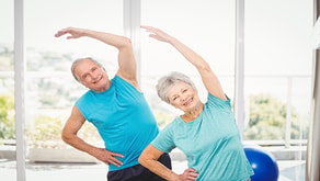 Two older adults in blue shirts engage in a healthcare training session with side stretches, highlighted by a Medbridge exercise ball.