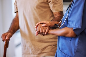 A healthcare worker in blue scrubs helps an elderly person, highlighting Medbridge's digital advancements.