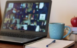 A laptop with a video call next to a notebook, blue mug, and red apple showcases medbridge's hybrid care technology for remote healthcare education.