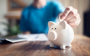A person drops a coin into a white piggy bank, symbolizing investment in medbridge's personalized healthcare software.