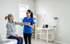 A physical therapist aids an older woman with arm exercises using medbridge software.