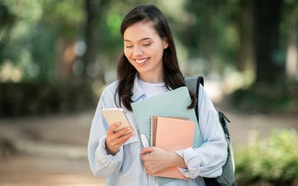A young woman stands outside, smiling at her phone while engaging with Medbridge digital healthcare education.