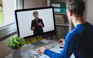 A man observes a woman discussing healthcare training on medbridge via a computer.
