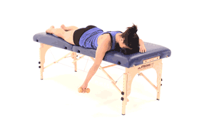 A person performs a shoulder exercise with a small dumbbell on a massage table, integrating digital healthcare, including medbridge, into their routine.