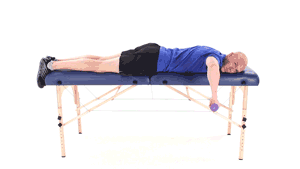 A person performs a dumbbell exercise on a massage table, blending fitness and therapy, for medbridge training.