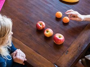 Two people sit at a wooden table with apples, tangerines, and a pink notebook.