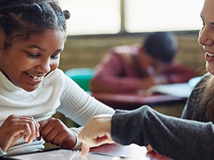 A student happily uses a tablet at a desk with their teacher in a Medbridge classroom.
