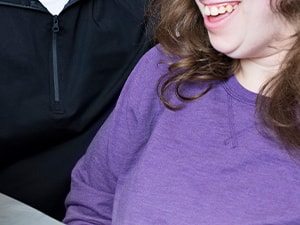 Two individuals smile at a blue tablet on the table, one wearing a black jacket and the other in a purple shirt, while using medbridge.