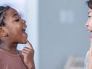 A child and adult practice speech by pointing to their open mouths.