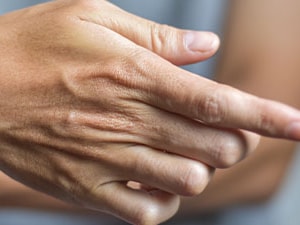 Individual clasping their right hand with the left, set against a plain background.