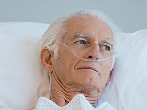 Elderly man with nasal cannula in hospital bed, looking sideways.