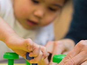 A child plays with a pegboard toy as an adult provides guidance.