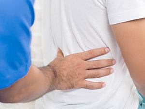 Someone in a blue shirt touches another person's back, against a white brick wall.