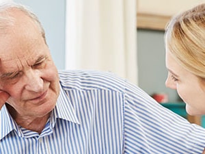 Nurse attentively supporting an elderly male patient showing signs of confusion in a home care setting.