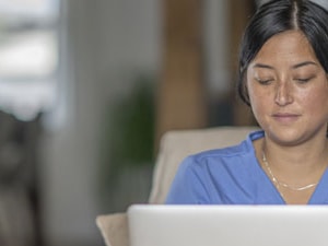 Individual in a blue shirt using a laptop on a beige couch, Medbridge setting.
