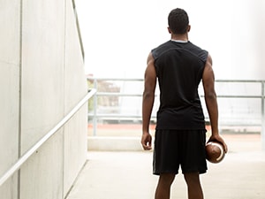 In athletic gear, a person stands in a well-lit passage with a football, back turned.