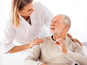 A woman in a white coat smiles at an elderly man on a couch in a warmly lit room, symbolizing care from medbridge.