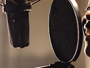 Individual with headphones speaking or singing into a microphone at a recording studio for medbridge.