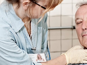 A medbridge healthcare worker checks the pulse of a calm older man in light blue attire.