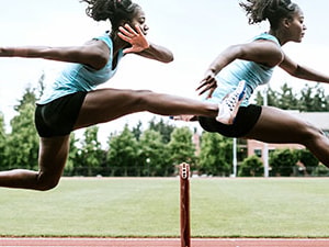An athlete in sportswear leaps over a hurdle on a track.