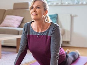 A woman practices cobra pose on a yoga mat in a living room.