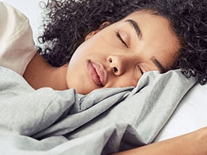 Woman peacefully sleeping in bed with soft lighting, representing sleep hygiene and restorative rest strategies.