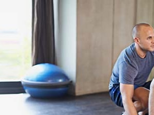 An older man is assisted by a younger man while sitting on an exercise ball in a gym, as seen on medbridge.