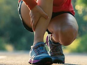 A person kneeling on a road holds their leg in discomfort against a natural background.
