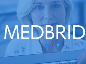 A laptop screen with a medbridge logo shows a video call with a woman and a hand near the keyboard.